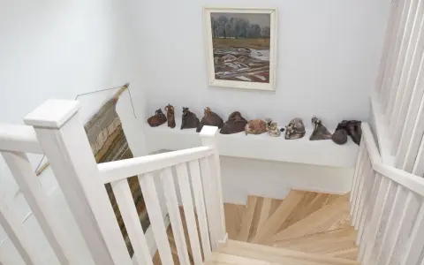 Klatka schodowa inspiracje: białe balustrady, drewniane stopnie i galeria ceramicznych rzeźb na półce.