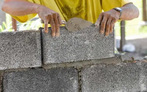 Budowniczy układa bloczki betonowe na zaprawie, tworząc solidny fundament.