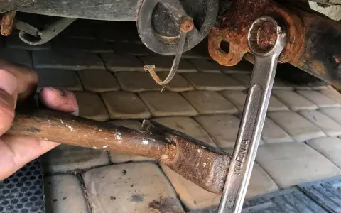 Ręka trzyma młotek, by pomóc odkręcić śrubę z zepsutym gwintem. Klucz nasadowy jest na śrubie.