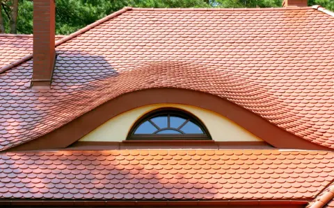 Dachówki ceramiczne w kolorze ceglastym pokrywają dach z charakterystycznym lukarną w kształcie oka.