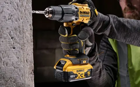 Mężczyzna w rękawicach wierci w betonie najmocniejszą wkrętarką DeWalt 18V XR.