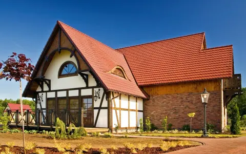 Elegancki dom z charakterystycznym dachem pokrytym czerwoną dachówką karpiówką, otoczony zadbanym ogrodem.