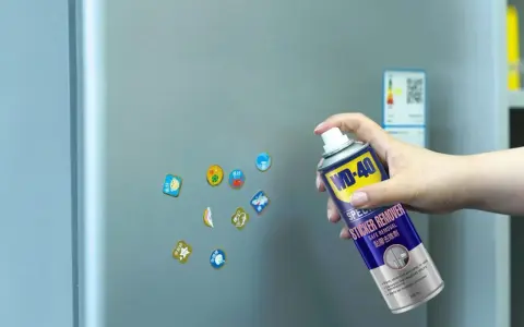 Jak usunąć naklejkę z szyby? Puszka WD-40 Sticker Remover w dłoni, gotowa do działania na lodówce.