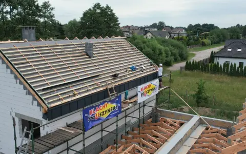 Budowa dachu z blachą i membraną. Pracownik na rusztowaniu montuje pokrycie.