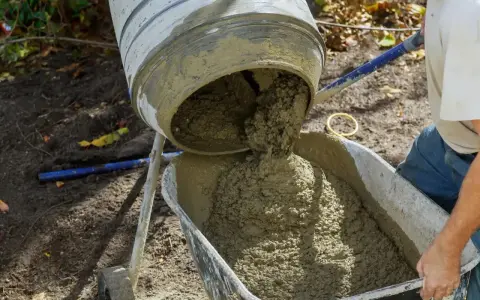 Świeża porcja betonu z betoniarki trafia do taczki, gotowa do dalszych prac budowlanych.